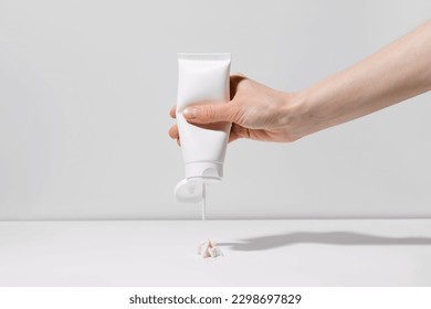 A female hand squeezes a body cream or scrub from a blank tube on a white plain background. Cosmetic product and self care concept. Place for your design - Powered by Shutterstock