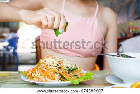 Female hand squeezing lime on Thai green papaya salad