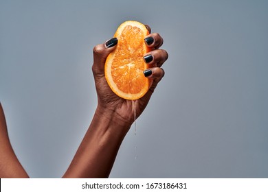 Female hand squeezing orange isolated on grey. Copy space