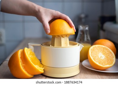 Female hand squeezing orange juice from fresh oranges with a juicer in the home kitchen, ?lose up.