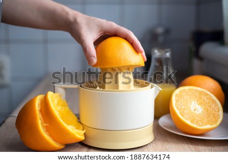 Female hand squeezing orange juice from fresh oranges with a juicer in the home kitchen, ?lose up.