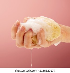 A Female Hand Squeezing Water Out Of A Natural Sea Sponge Body Care On A Feminine Pink Background