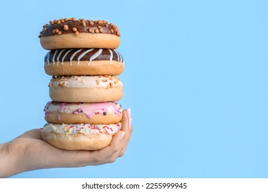 Female hand with stack of tasty donuts on color background, closeup