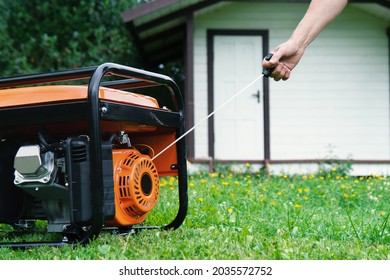 Female hand starts a portable electric generator standing on the grass in front of a summer house in summer evening - Shutterstock ID 2035572752