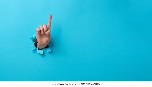female hand sticking out of a torn hole in a blue paper background, attention gesture. Place for an inscription, banner
