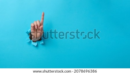 female hand sticking out of a torn hole in a blue paper background, attention gesture. Place for an inscription, banner