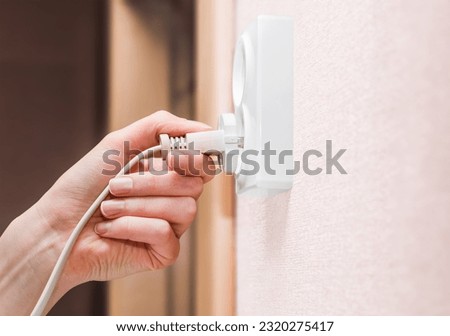female hand sticks an electric plug into a socket, side view