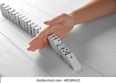 Female Hand Stopping Domino Effect On Wooden Table