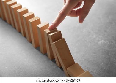 Female Hand Stopping Domino Effect On Grey Background