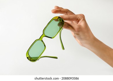 Female hand with stylish sunglasses on light background