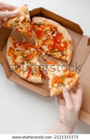 Female hand take piece of mexican pizza in cardboard box for delivery on white solid background. Top view
