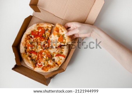 Female hand take piece of mexican pizza in cardboard box for delivery on white solid background. Top view