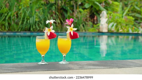 Female hand takes a cool cocktail near to swimming pool. Couple of glasses of orange juice on blue water background. Summer day bright juicy lemonade. Close-up footage. - Powered by Shutterstock