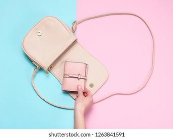 Female hand takes leather wallet from bag on pastel background. Top view, flat lay, minimalism