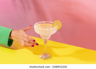 Female hand taking glass of delicious margarita cocktail isolated over pink yellow background. Concept of cocktails, alcoholic drinks, taste, party, mix. Copy space for ad. Retro style - Powered by Shutterstock