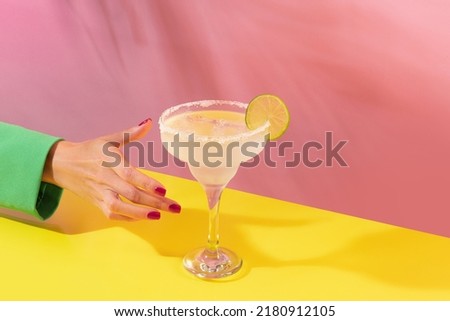 Female hand taking glass of delicious margarita cocktail isolated over pink yellow background. Concept of cocktails, alcoholic drinks, taste, party, mix. Copy space for ad. Retro style
