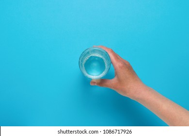 Female Hand Taking A Glass Of Water On A Blue Background. Flat Lay Still Life Table Top View Blue Background.