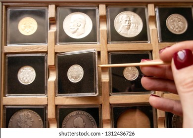 Female hand taking out a metal coin in a transparent plastic protection square capsule from a wooden display case with numismatic collection with a wooden stick. Coin holder case for numismatist.