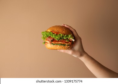 Female hand with tasty burger on color background