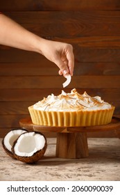 Female hand with tasty coconut pie on wooden background