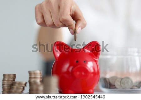 Female hand throwing cash coins into red piggy bank closeup. Home bookkeeping concept