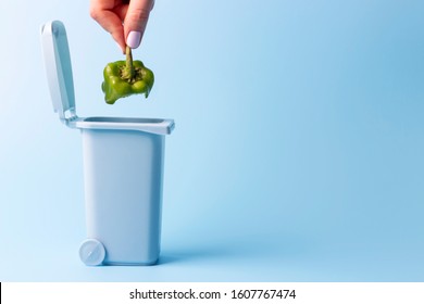 Female Hand Throws Food Trash Into Trash Can On Blue Background, Copy Space