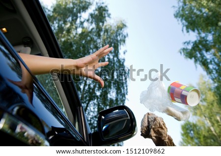 a female hand throws a handful of garbage accumulated in the car through the open window of the car - coffee glasses, bags, crumpled paper. Flying objects are slightly blurred to enhance the effect of