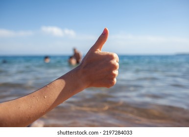 Female Hand Thumbs Up On Sea And Sky Background Closeup. Woman Showing Ok Sign On Shoreline Coastline. Body Language, Communication Concept. Holiday, Vacation, Summer Is Coming Conceptual Photo.