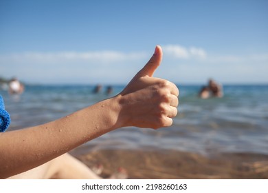 Female Hand Thumbs Up On Sea And Sky Background Closeup. Woman Showing Ok Sign On Shoreline Coastline. Body Language, Communication Concept. Holiday, Vacation, Summer Is Coming Conceptual Photo.