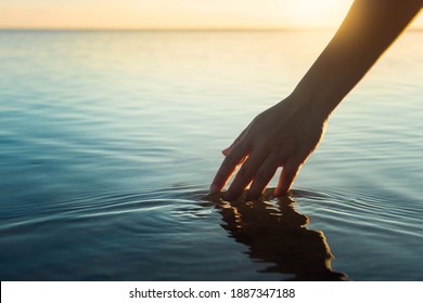 A female hand touching the ocean water in front of a beautful sunset during summer time. - Shutterstock ID 1887347188