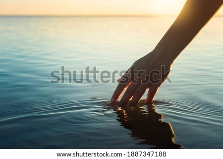 A female hand touching the ocean water in front of a beautful sunset during summer time. Stockfoto © 