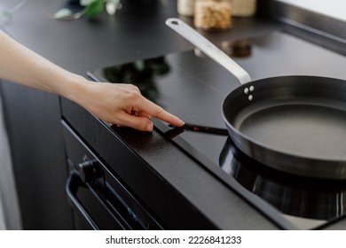 female hand touching sensor button on control panel of electrical hob and cooking dinner on frying pan at home kitchen, modern household appliance 