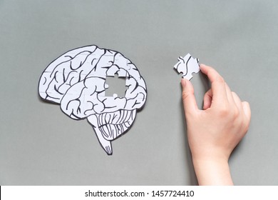 Female hand trying to connect a missing jigsaw puzzle of human brain on gray background. Creative idea for solving problem, memory loss, dementia or Alzheimer's disease concept. Mental health care.