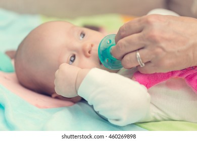 Female Hand Trying To Put A Green Pacifier Into Baby Girl's Mouth, Instagram Filter Applied In Post Processing