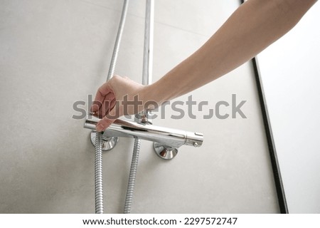 Female hand turn on shower faucet. Modern shower set in bathroom interior. Hygiene concept