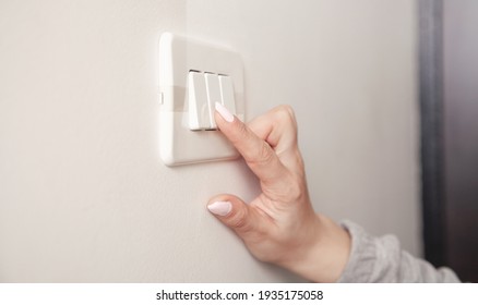 Female Hand Turning An Electricity Light Switch On The Wall.