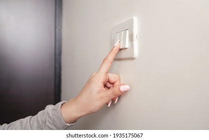 Female Hand Turning An Electricity Light Switch On The Wall.