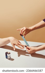Female hand using nail file, taking care after hands, nails against beige background. Professional salon manicure. Concept of hand care, cosmetics and cosmetology, spa, natural beauty. Poster, ad