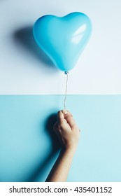 Female Hand Using Scissors To Free A Blue Heart Balloon, Pastel Background, Trendy Pop Concept