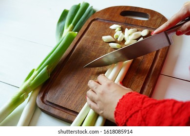 Female hand using sharp knife to cut Negi (Japanese Long Onion) or Japanese Scallion, Bunching Onion, Green Onion on wooden cutting board over white painted wood planks background. (top view)