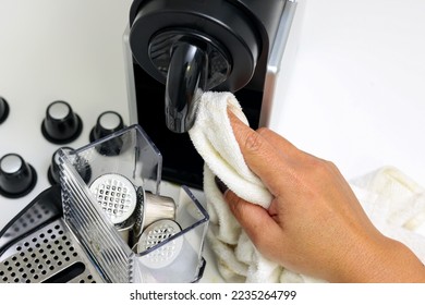 Female hand using white kitchen towel cleaning an automatic espresso machine with used coffee capsules in the blurred background.