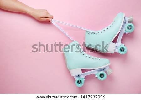 Female hand and vintage roller skates on color background