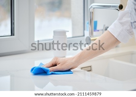 Female hand with washing sponge cleaning stone surface of kitchen tabletop (photo with shallow depth of field)