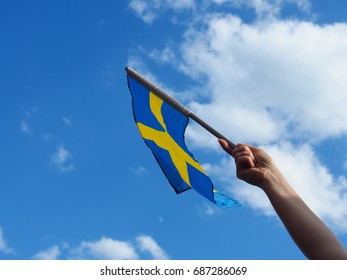 Female hand waving with the Swedish flag on a blue summer sky
