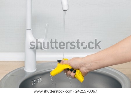 female hand wets a rag under running water in the kitchen. woman wets a rag in water. wet kitchen cleaning