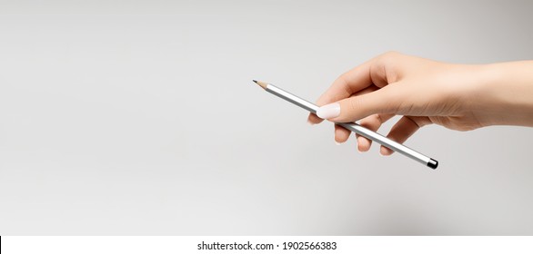 Female hand with white nail design. White nail polish manicure. Female hand hold silver pencil on gray background