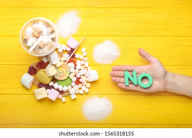 Female hand with word NO and many sweets on color background