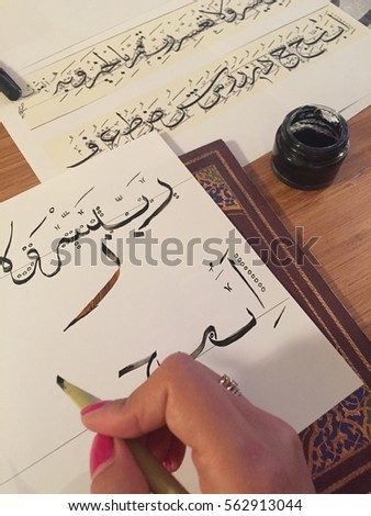 Female hand writing Arabic alphabet letters with wooden calligraphy pen and black ink.
