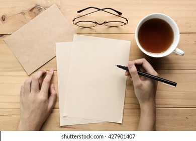 Female Hand Writing Down On Letter Paper With Cup Of Tea On The Wood Desk, Top View