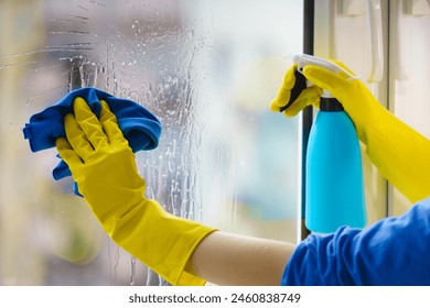 Female hand in yellow gloves cleaning window pane with rag and spray detergent. Cleaning concept